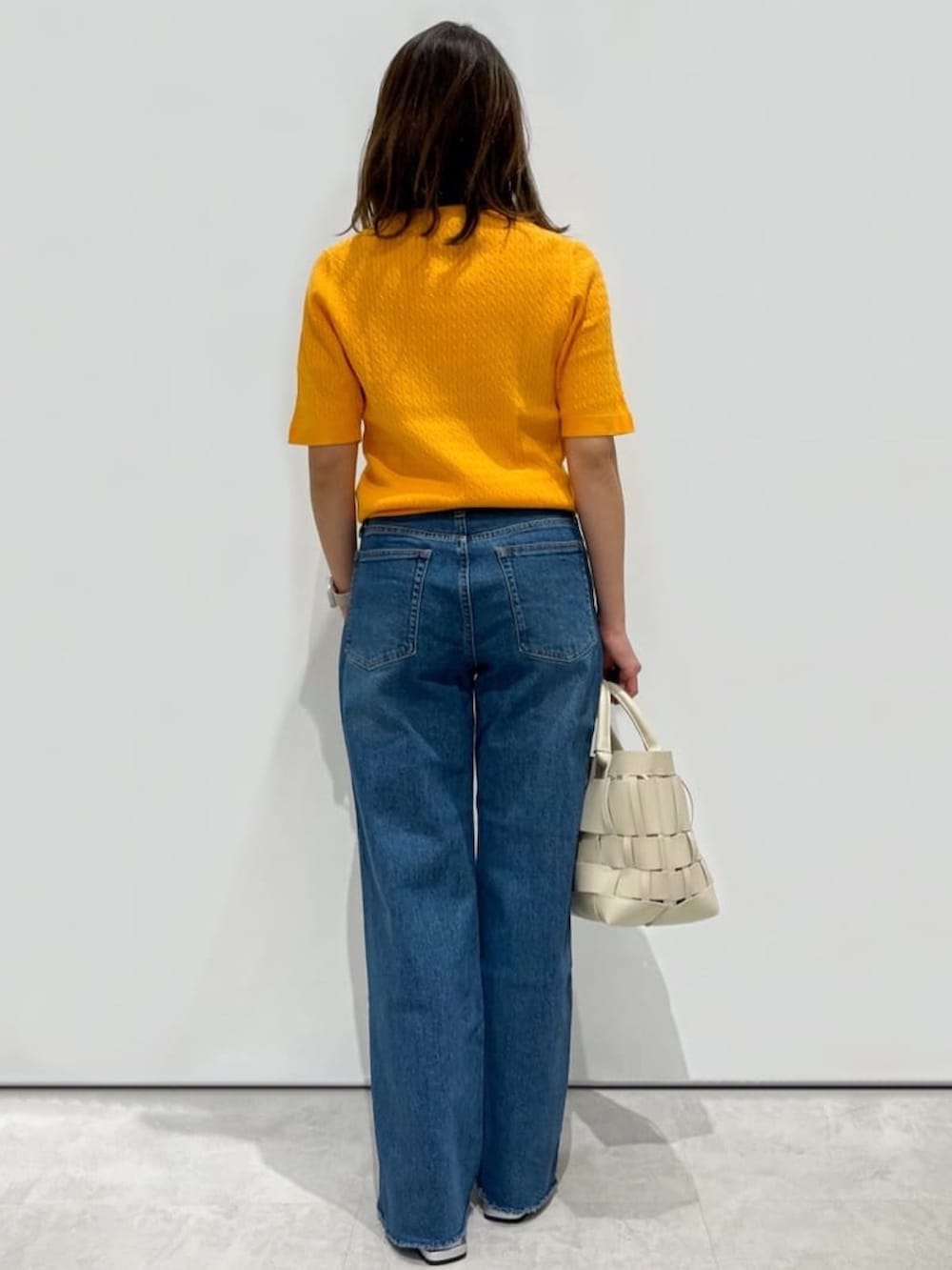 オレンジ系のニット/セーター、ブルー系のデニムパンツ、ホワイト系のトートバッグを着用したレディースの夏コーディネートの2枚目の写真