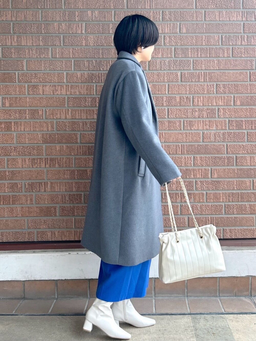 ブルー系のスカート、グレー系のニット/セーター、グレー系のチェスターコートを着用したレディースの秋コーディネートの4枚目の写真
