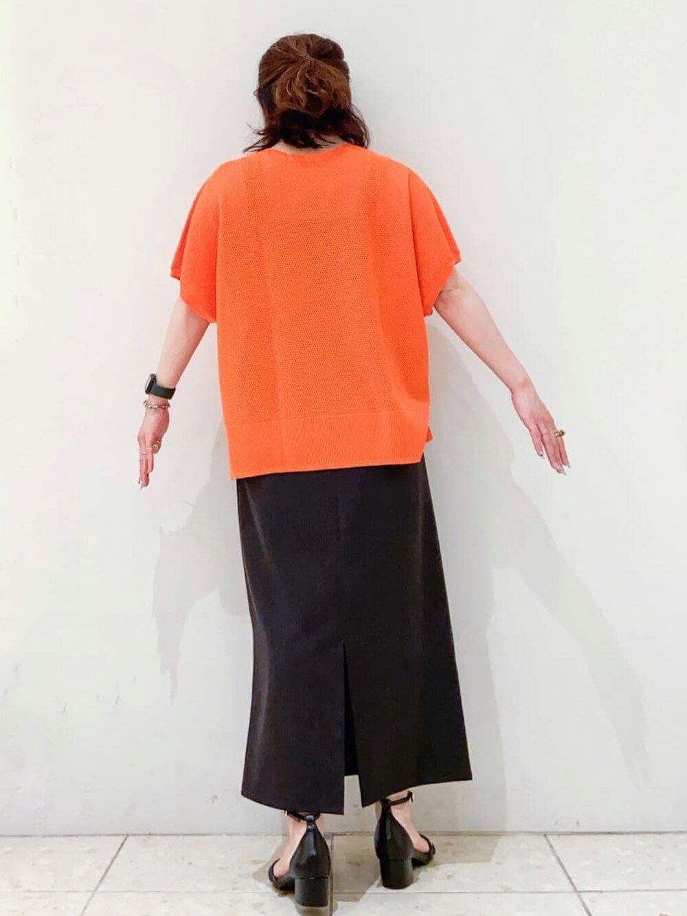 オレンジ系のニット/セーター、グレー系のスカート、ブラック系のショルダーバッグを着用したレディースの夏コーディネートの3枚目の写真