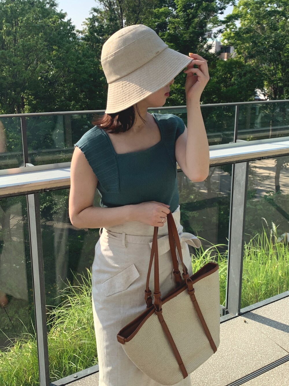 グリーン系のニット/セーター、ホワイト系のスカート、ベージュ系のトートバッグを着用したレディースの夏コーディネートの2枚目の写真