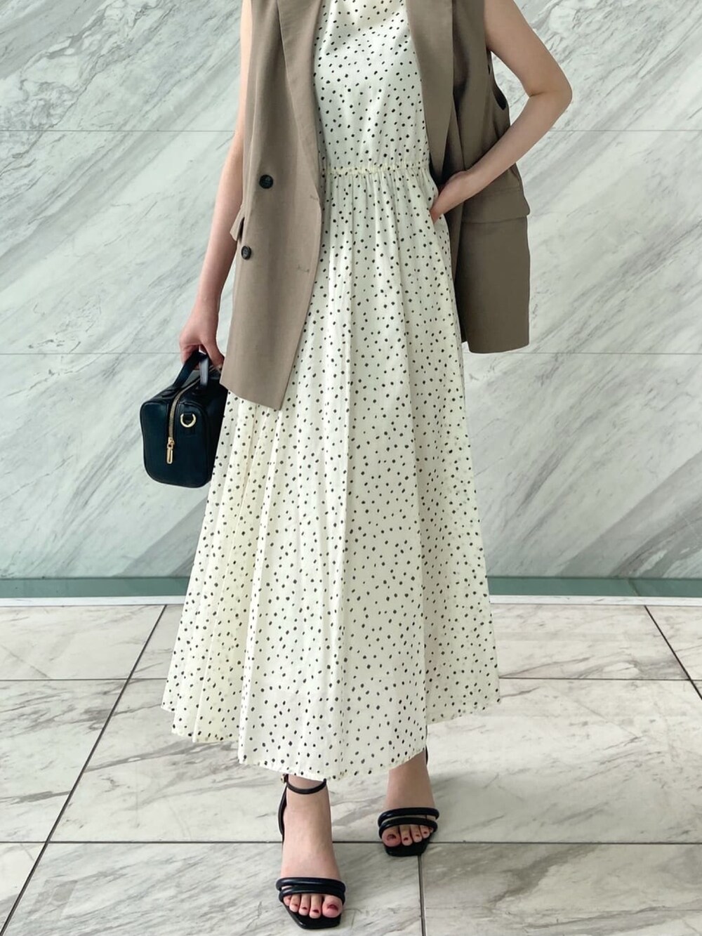 ブラウン系のベスト、ホワイト系のワンピース、ブラック系のサンダルを着用したレディースの春コーディネートの9枚目の写真