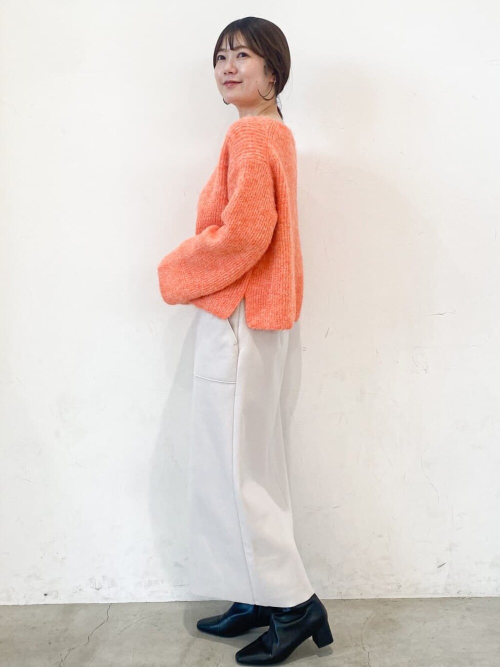 ブラック系のチェスターコート、オレンジ系のニット/セーター、ベージュ系のスカートを着用したレディースの冬コーディネートの6枚目の写真