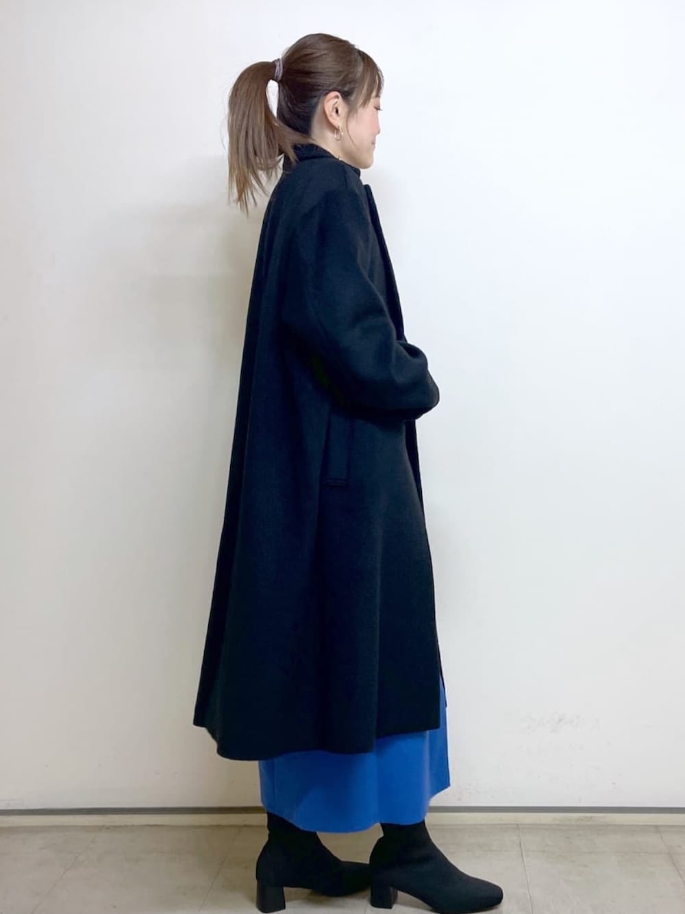 ブラック系のチェスターコート、ブルー系のスカート、ブラック系のブーツを着用したレディースの冬コーディネートの2枚目の写真