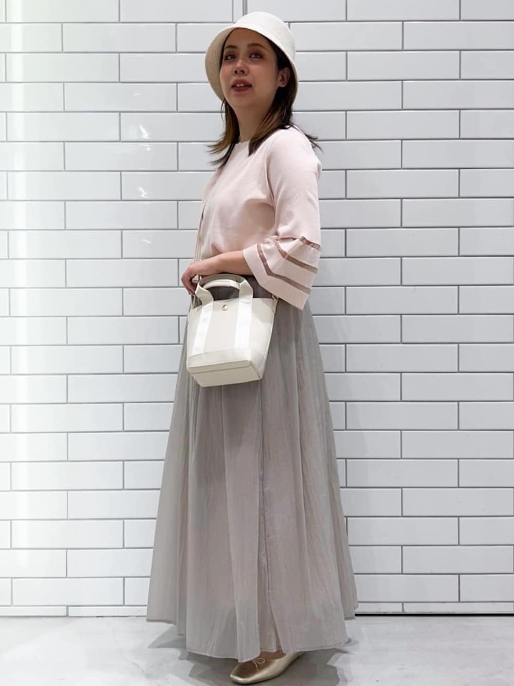 ピンク系のニット/セーター、ベージュ系のスカート、ゴールド系のパンプスを着用したレディースの春コーディネートの2枚目の写真