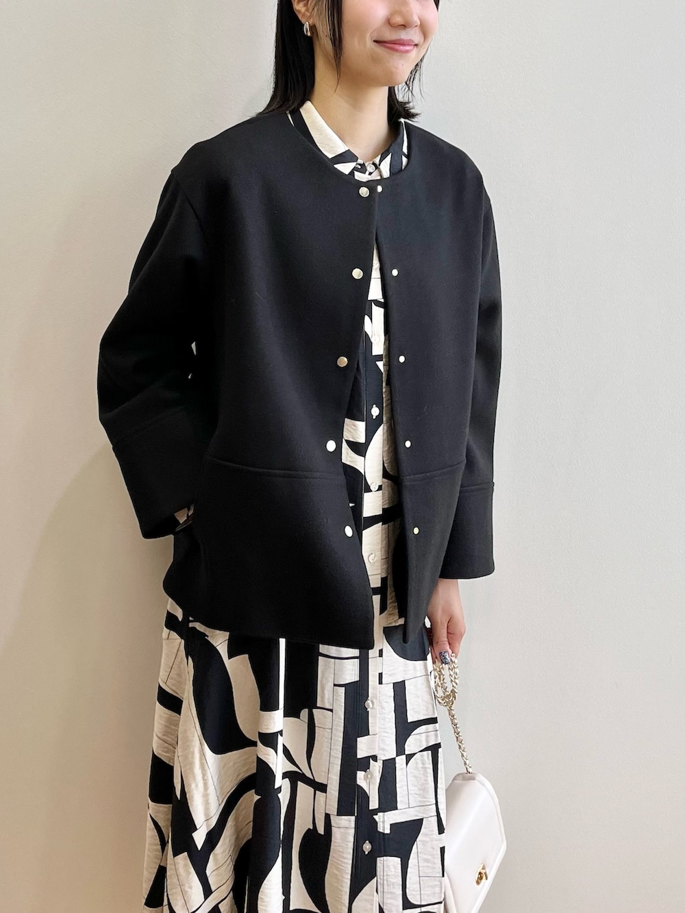 ブラック系のノーカラーコート、ベージュ系のワンピース、ブラック系のブーツを着用したレディースの秋コーディネートの5枚目の写真