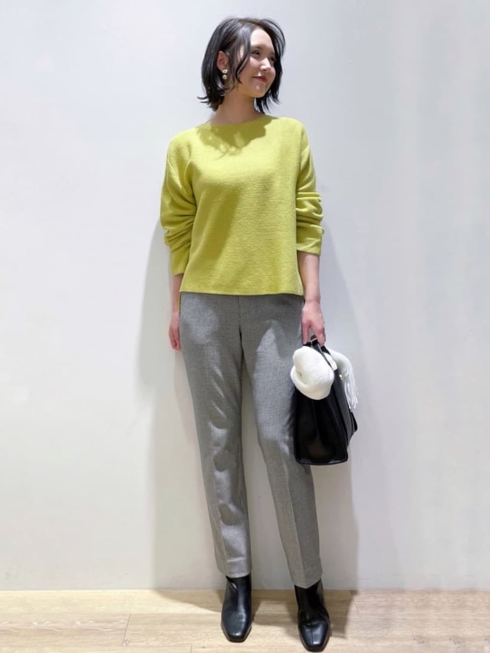 ブラック系のノーカラーコート、イエロー系のニット/セーター、ブラック系のトートバッグを着用したレディースの秋コーディネートの4枚目の写真