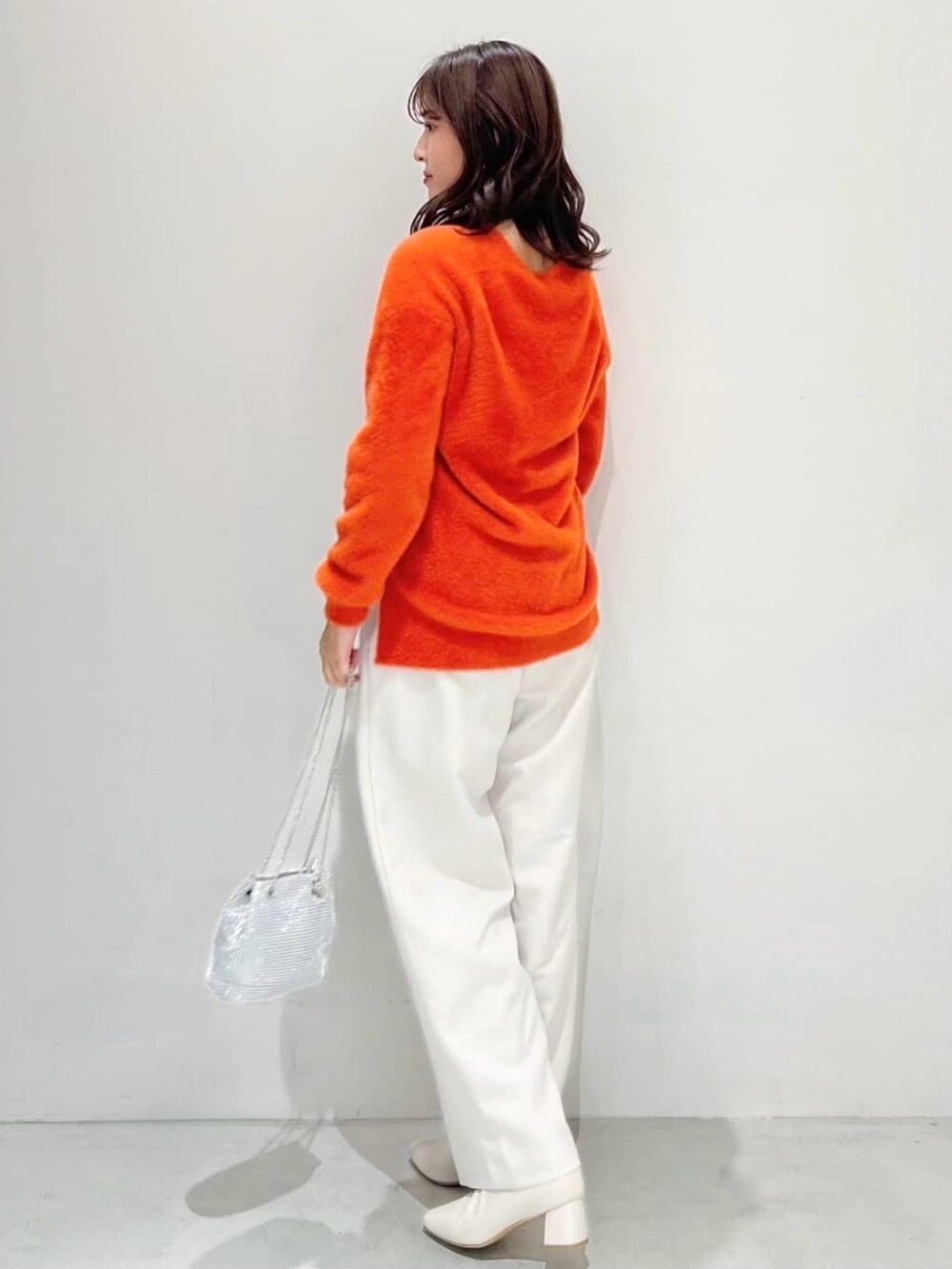 オレンジ系のニット/セーター、ホワイト系のその他パンツ、ホワイト系のショルダーバッグを着用したレディースの秋コーディネートの3枚目の写真