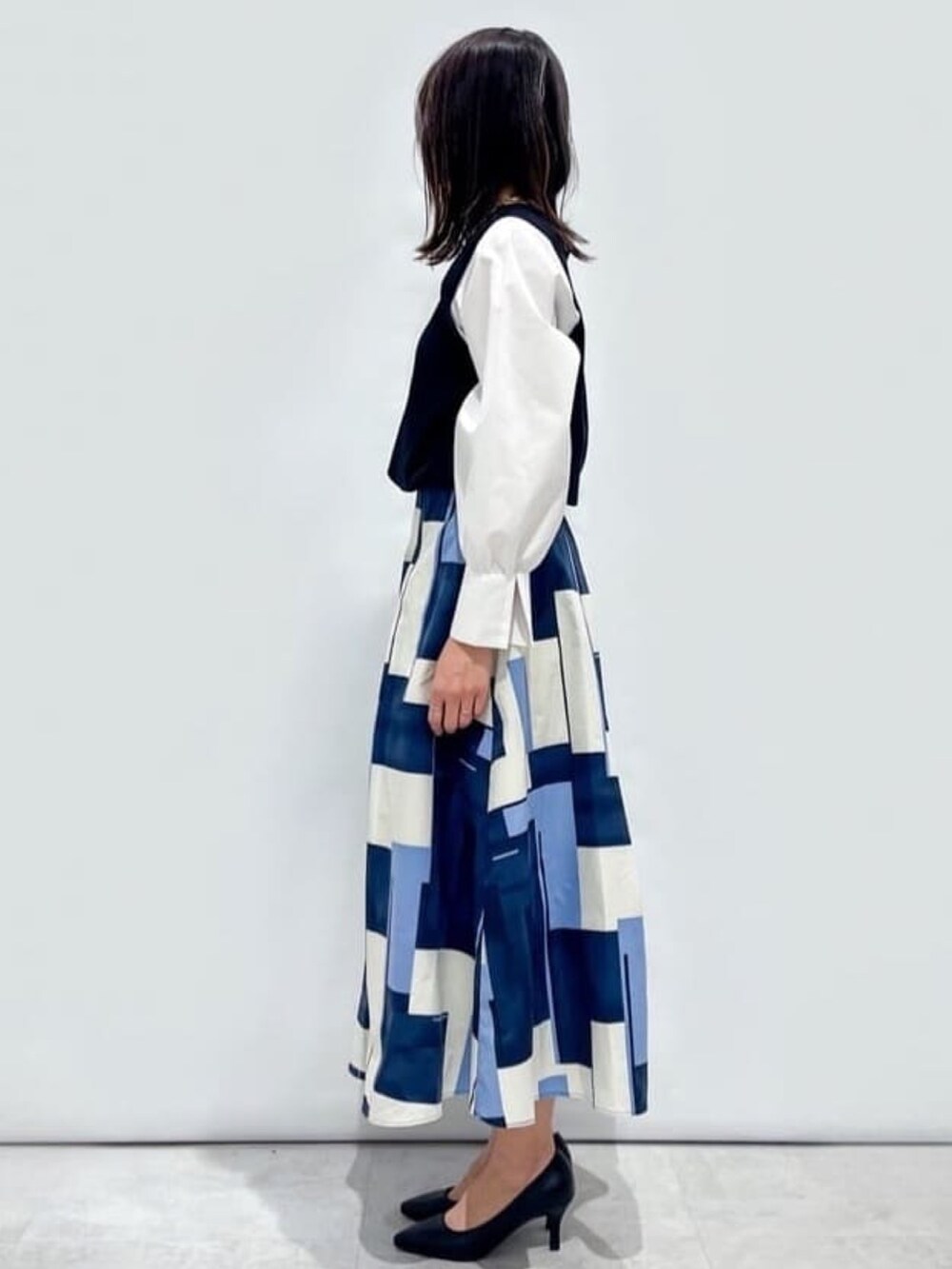 ブラック系のニット/セーター、ブルー系のスカート、ブラック系のショルダーバッグを着用したレディースの春コーディネートの2枚目の写真