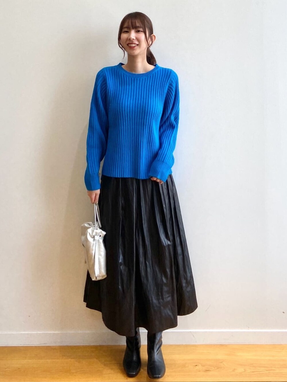 ブルー系のニット/セーター、ブラック系のスカート、ブラック系のブーツを着用したレディースの秋コーディネートの2枚目の写真