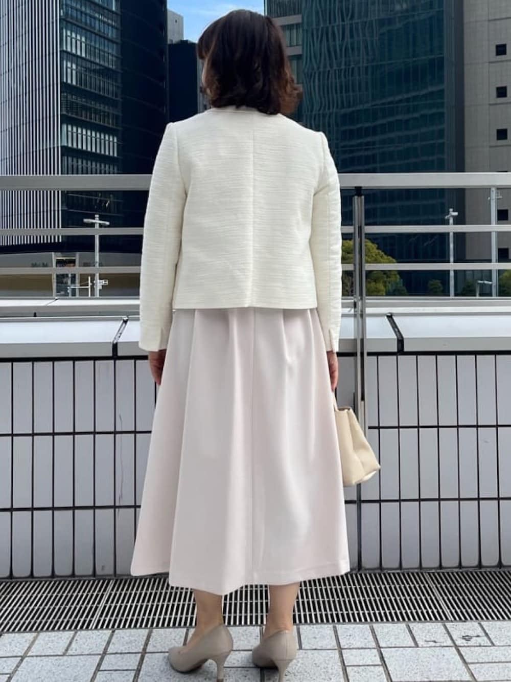 ホワイト系のノーカラージャケット、ベージュ系のワンピース、ベージュ系のパンプスを着用したレディースの冬コーディネートの3枚目の写真