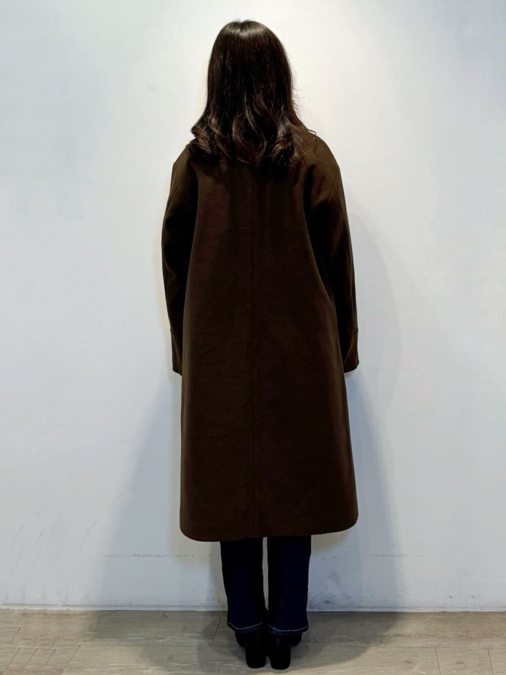 ブラウン系のノーカラーコート、ホワイト系のニット/セーター、ブルー系のデニムパンツを着用したレディースの冬コーディネートの4枚目の写真