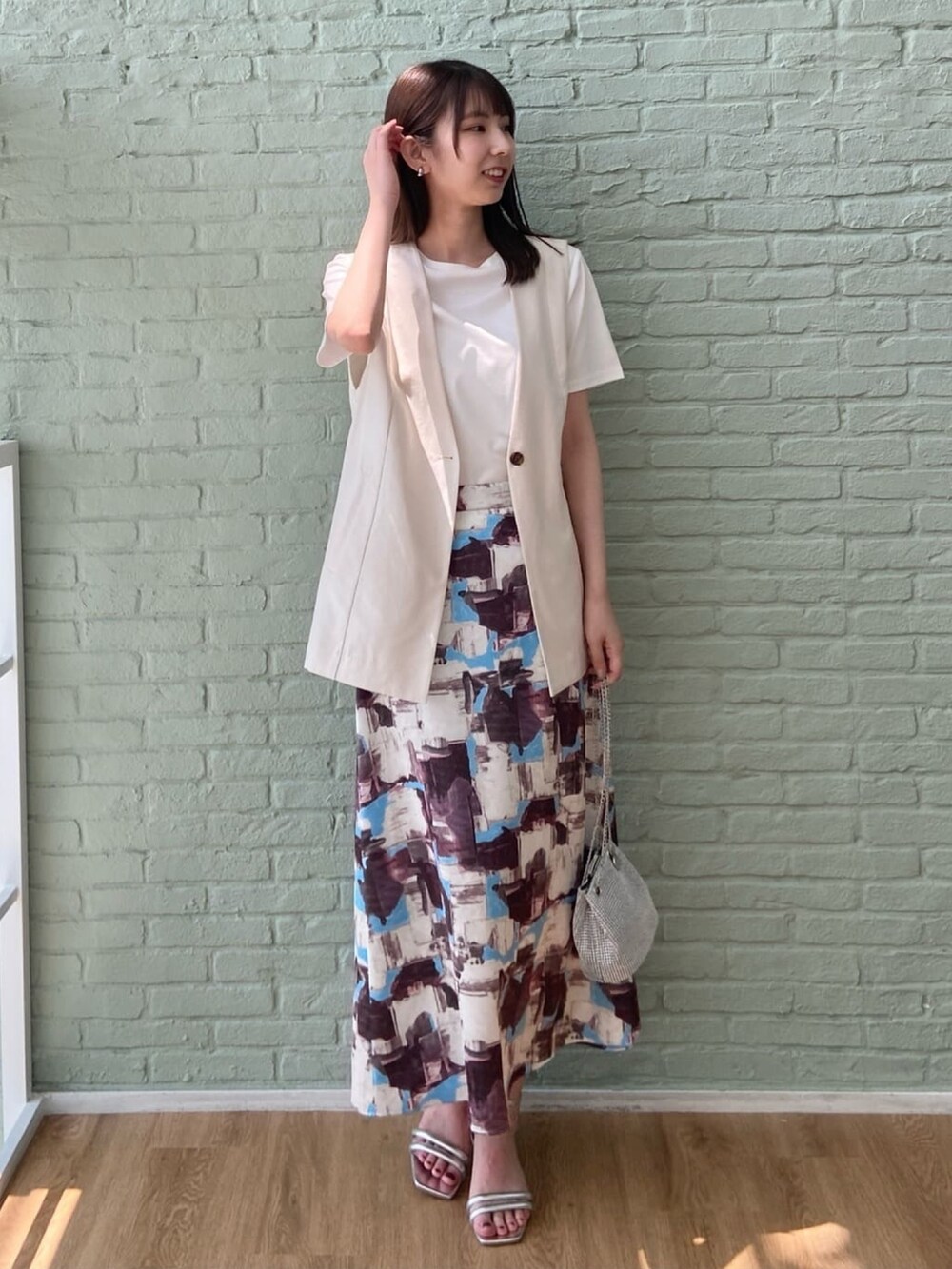 ベージュ系のベスト、ホワイト系のTシャツ/カットソー、レッド系のスカートを着用したレディースの夏コーディネートの3枚目の写真