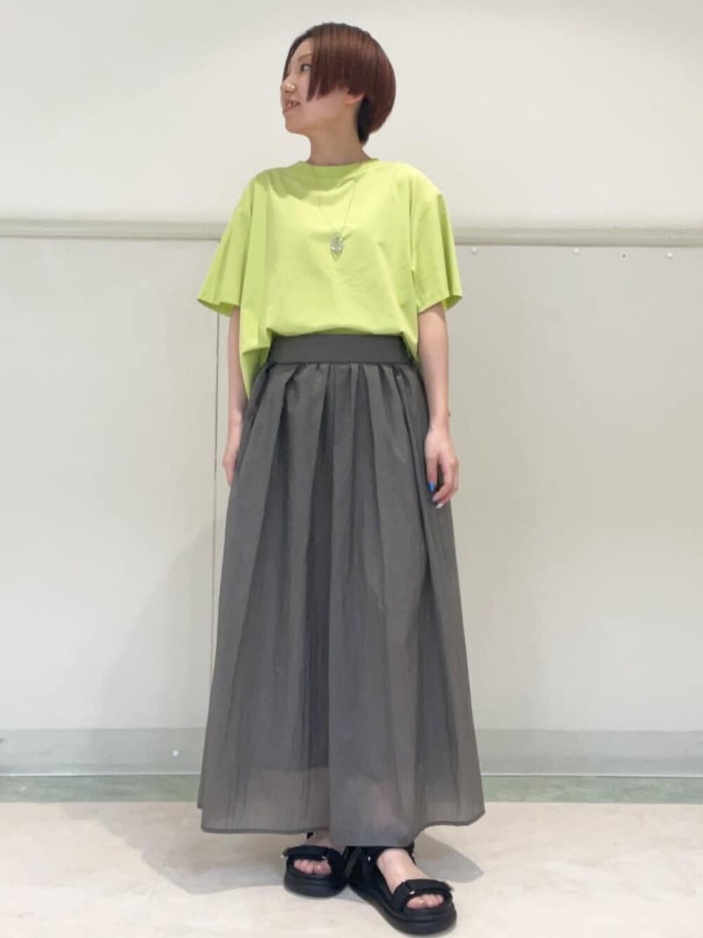 グレー系のスカート、ブラック系のサンダル、グリーン系のTシャツ/カットソーを着用したレディースの春コーディネートの2枚目の写真