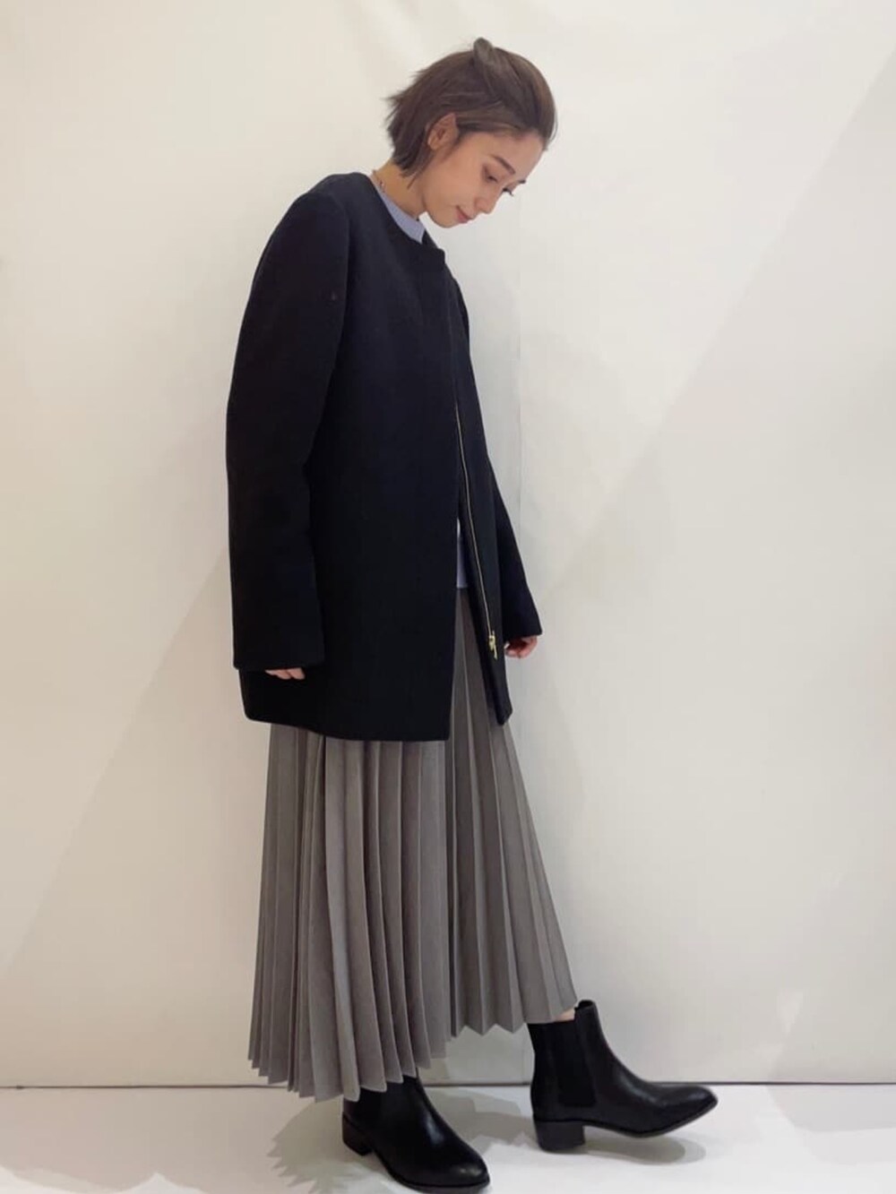 ブラック系のノーカラーコート、ブルー系のニット/セーター、グレー系のスカートを着用したレディースの冬コーディネートの3枚目の写真