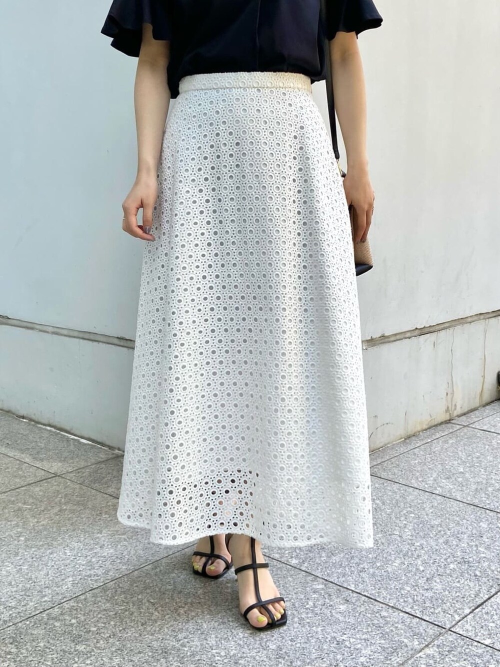 ブラック系のTシャツ/カットソー、ホワイト系のスカート、ブラック系のサンダルを着用したレディースの春コーディネートの5枚目の写真