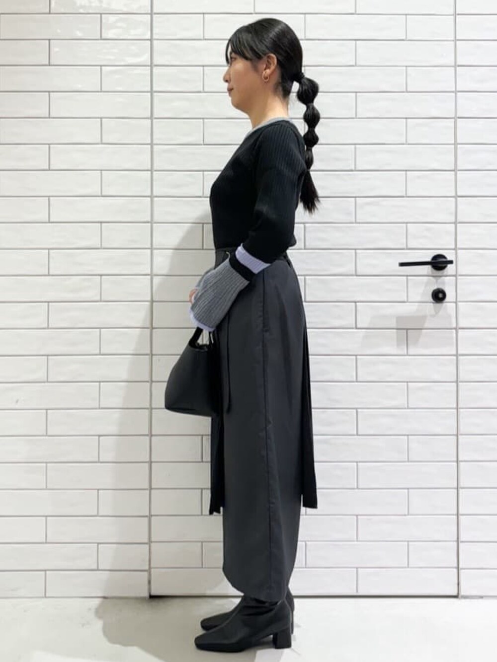 グレー系のニット/セーター、グレー系のスカート、ブラック系のトートバッグを着用したレディースの秋コーディネートの2枚目の写真