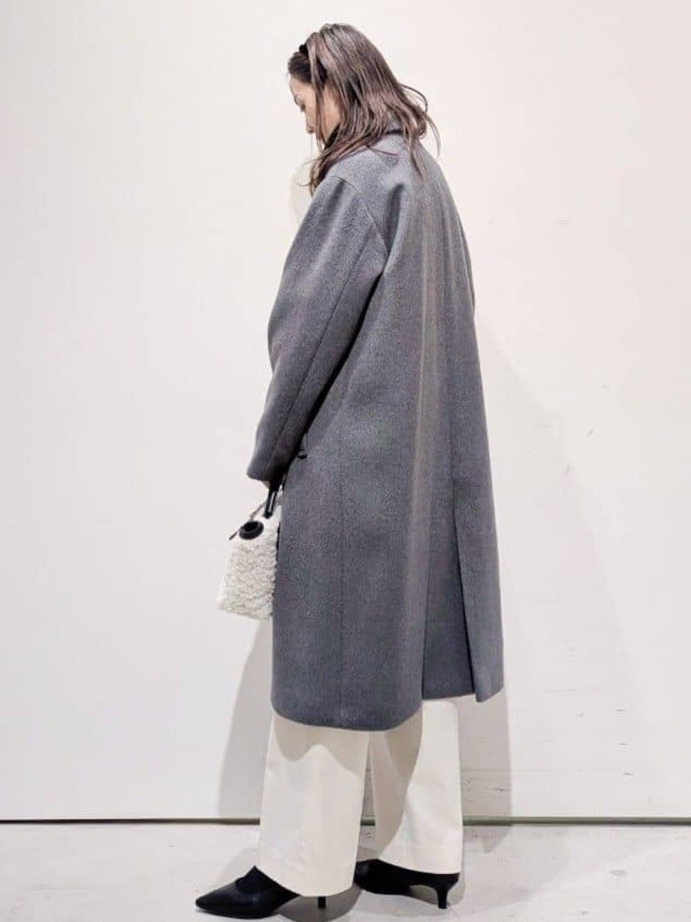 グレー系のチェスターコート、ホワイト系のその他パンツ、ブラック系のニット/セーターを着用したレディースの冬コーディネートの3枚目の写真