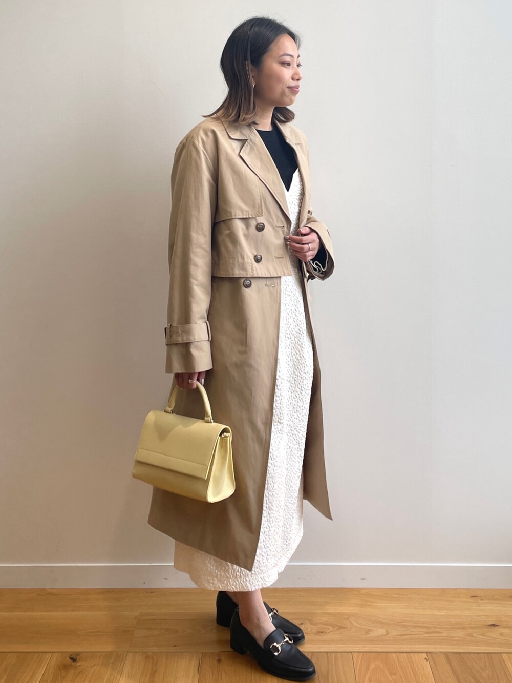 ベージュ系のトレンチコート、ホワイト系のワンピース、イエロー系のショルダーバッグを着用したレディースの春コーディネートの2枚目の写真