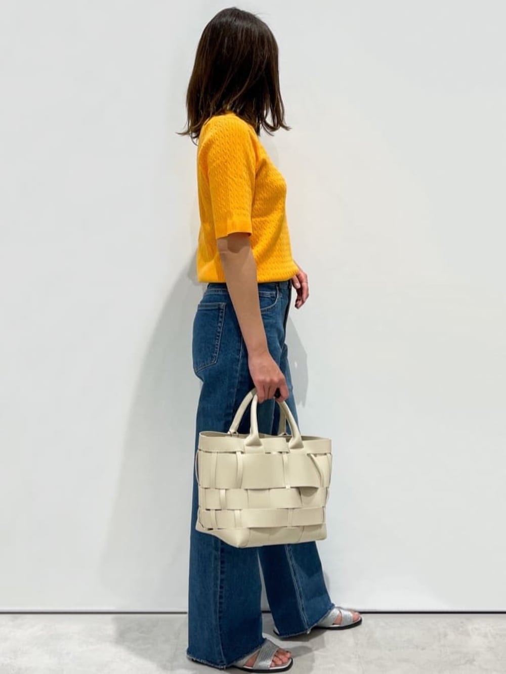 オレンジ系のニット/セーター、ブルー系のデニムパンツ、ホワイト系のトートバッグを着用したレディースの夏コーディネートの3枚目の写真