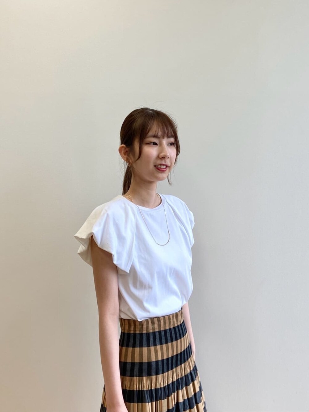 ベージュ系のスカート、ホワイト系のTシャツ/カットソー、ブラック系のサンダルを着用したレディースの夏コーディネートの6枚目の写真