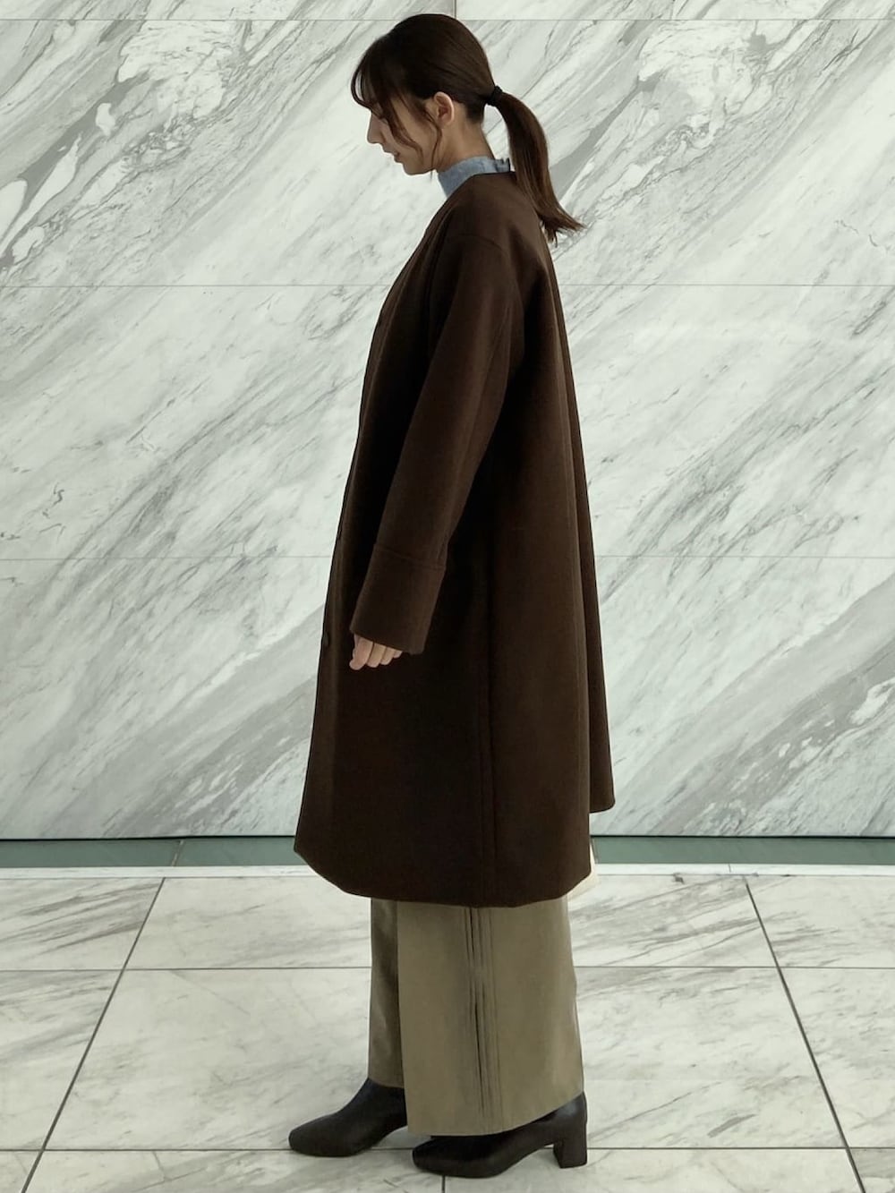 ブラウン系のノーカラーコート、ブラウン系のその他パンツ、ブルー系のニット/セーターを着用したレディースの秋コーディネートの3枚目の写真