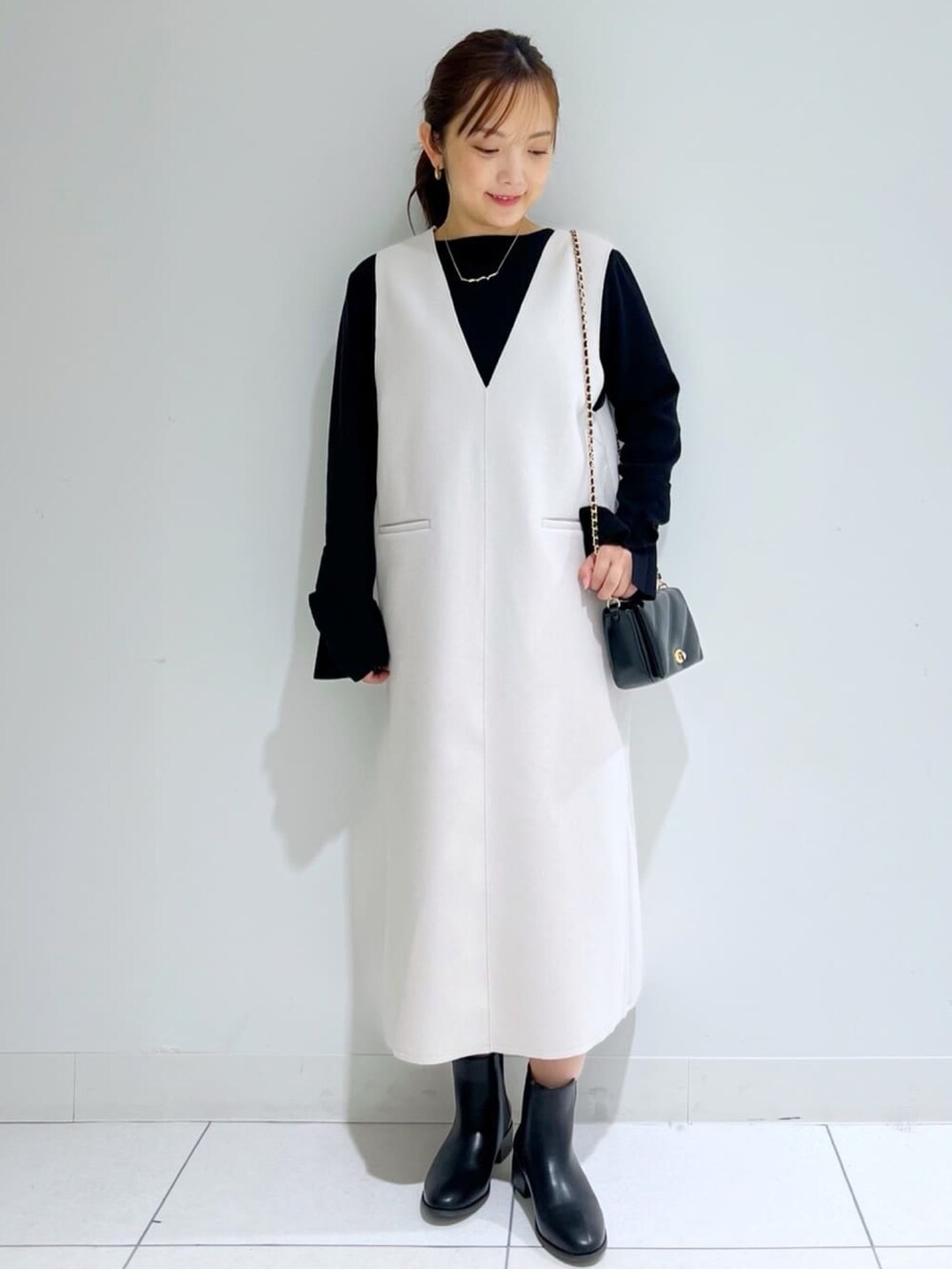ホワイト系のチェスターコート、ブラック系のショルダーバッグ、ブラック系のブーツを着用したレディースの冬コーディネートの2枚目の写真