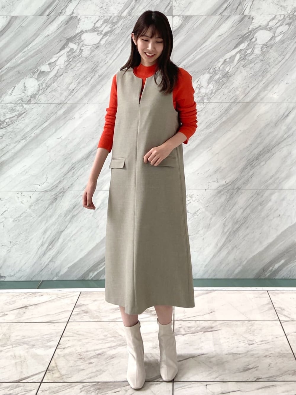 オレンジ系のニット/セーター、ベージュ系のワンピース、ホワイト系のブーツを着用したレディースの秋コーディネートの2枚目の写真