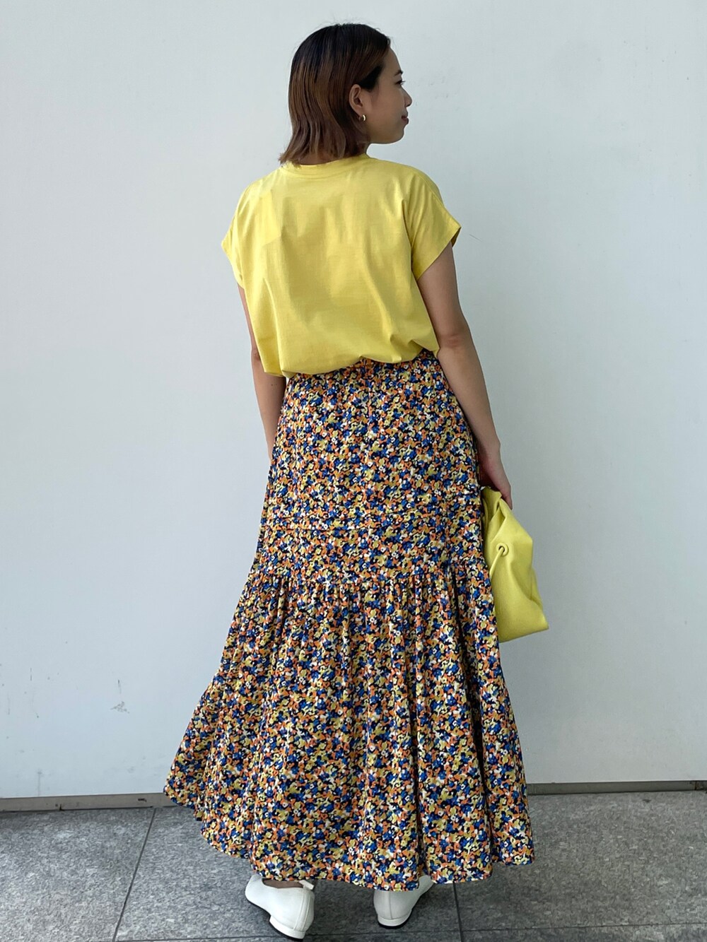 イエロー系のTシャツ/カットソー、オレンジ系のスカート、ホワイト系のパンプスを着用したレディースの夏コーディネートの3枚目の写真