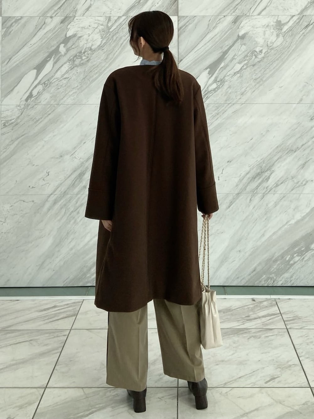 ブラウン系のノーカラーコート、ブラウン系のその他パンツ、ブルー系のニット/セーターを着用したレディースの秋コーディネートの4枚目の写真