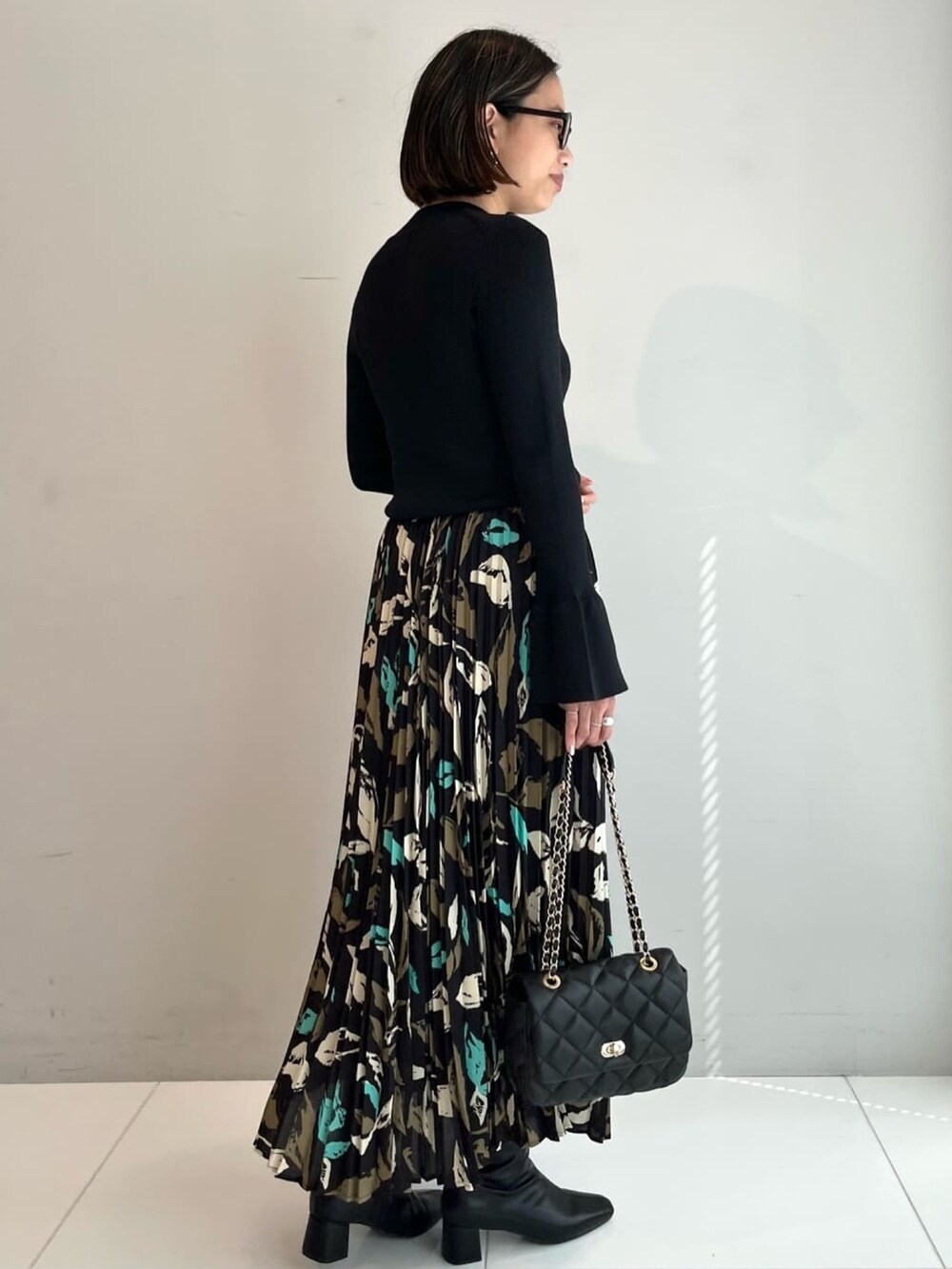 ブラック系のニット/セーター、ブラック系のスカート、ブラック系のショルダーバッグを着用したレディースの秋コーディネートの2枚目の写真