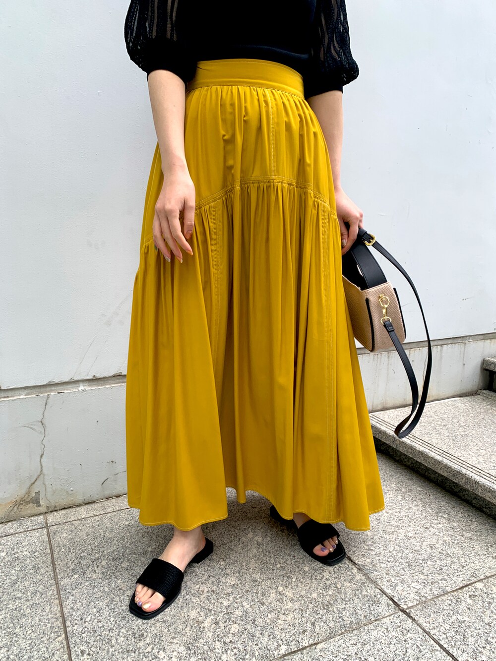 ブラック系のニット/セーター、イエロー系のスカート、ブラック系のショルダーバッグを着用したレディースの春コーディネートの3枚目の写真