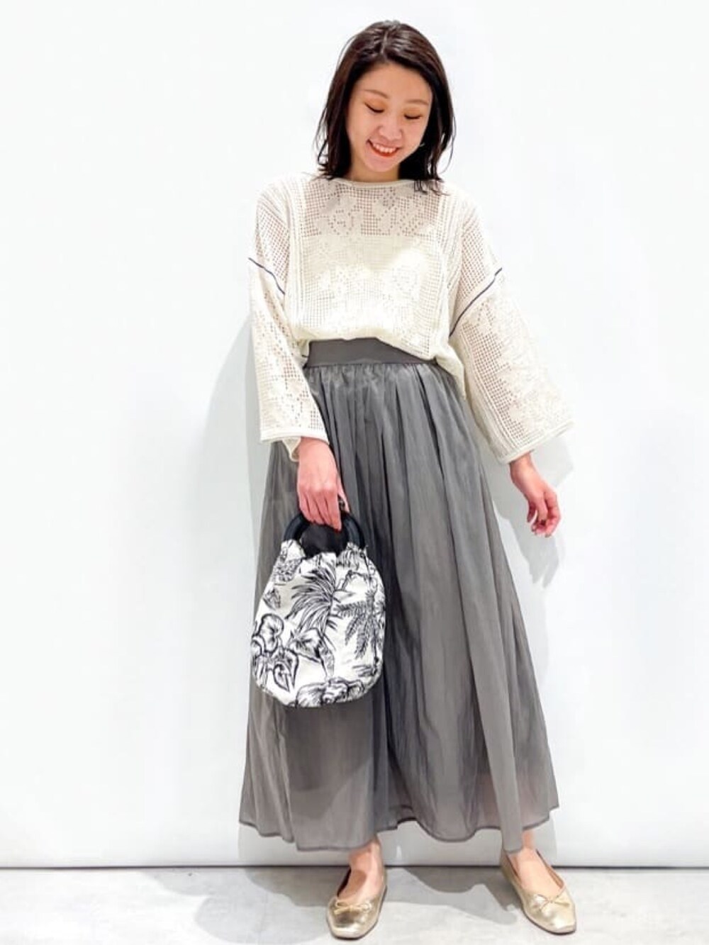 ホワイト系のニット/セーター、グレー系のスカート、ホワイト系のハンドバッグを着用したレディースの春コーディネートの2枚目の写真