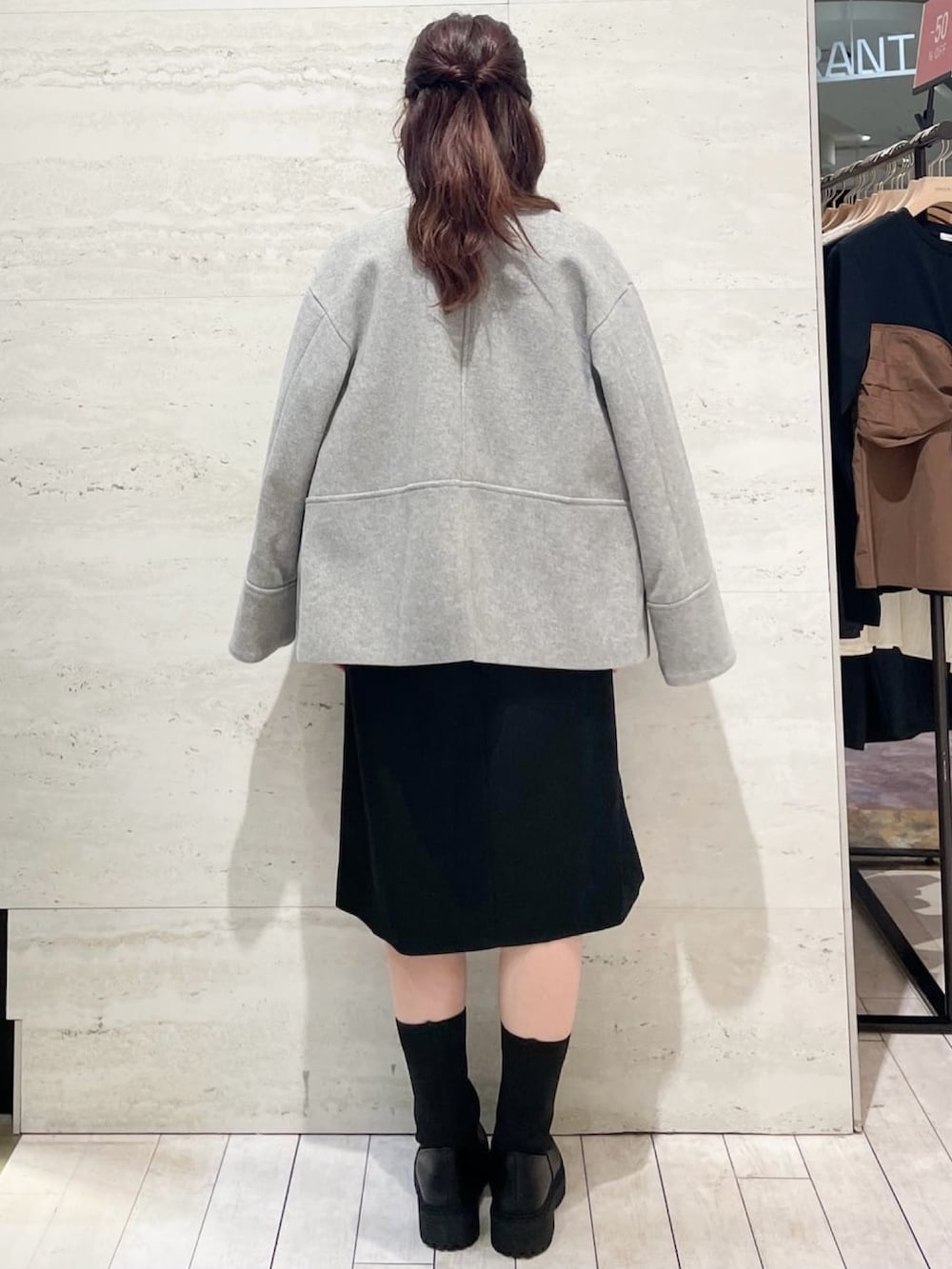 グレー系のノーカラーコート、オレンジ系のニット/セーター、ブラック系のワンピースを着用したレディースの冬コーディネートの2枚目の写真