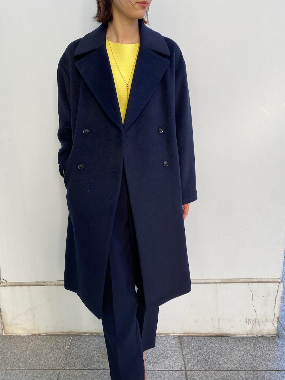 ブルー系のチェスターコート、イエロー系のニット/セーター、ベージュ系のブーツを着用したレディースの冬コーディネートの2枚目の写真