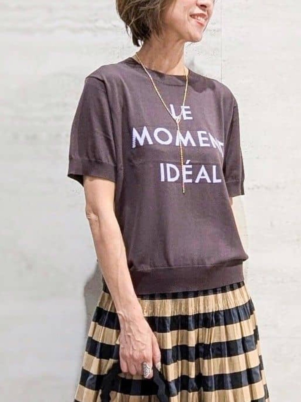 ブラウン系のニット/セーター、ベージュ系のスカート、ブラック系のハンドバッグを着用したレディースの夏コーディネートの2枚目の写真