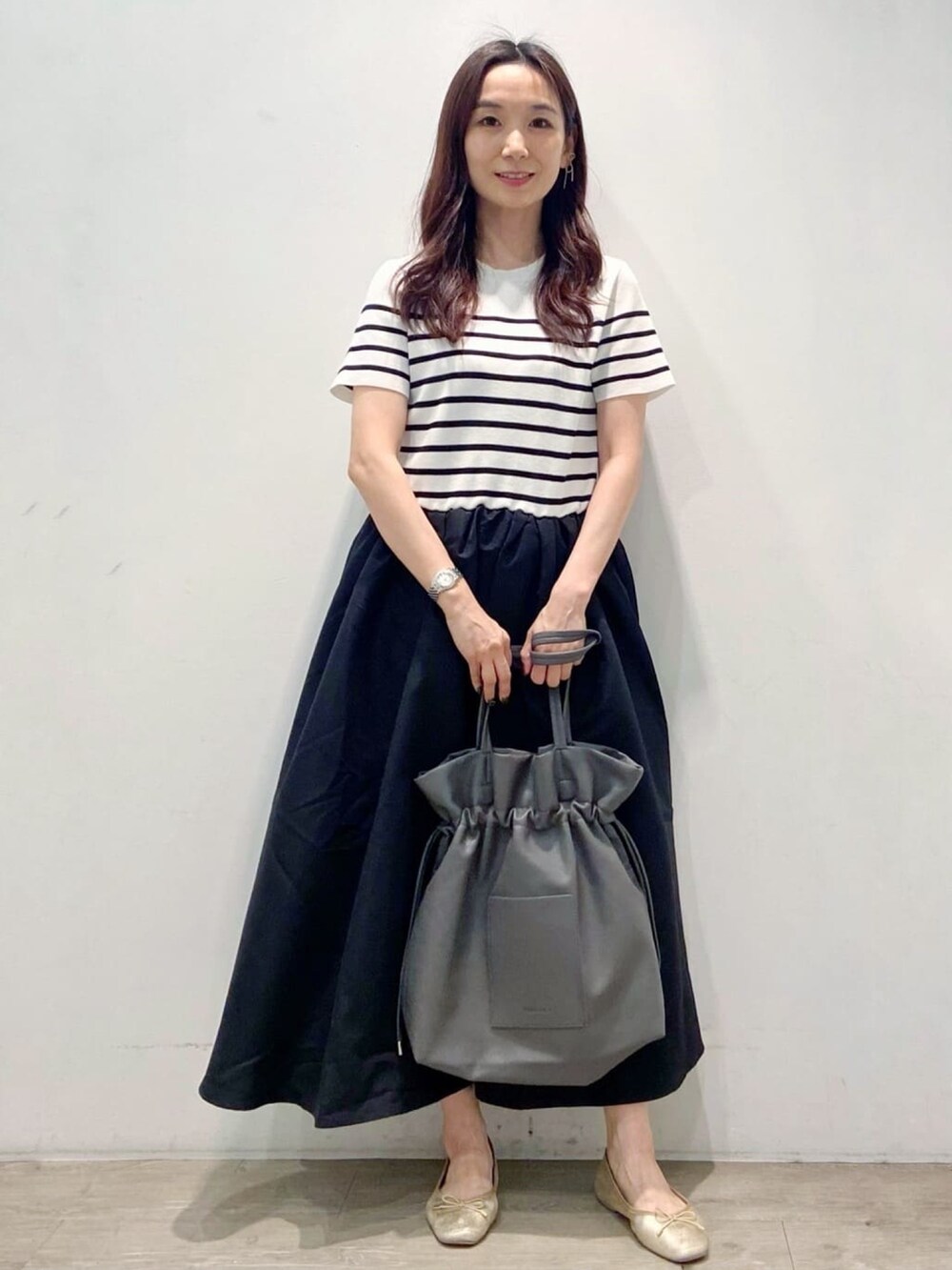 グレー系のトートバッグ、ブラック系のワンピース、ゴールド系のその他シューズを着用したレディースの夏コーディネートの3枚目の写真