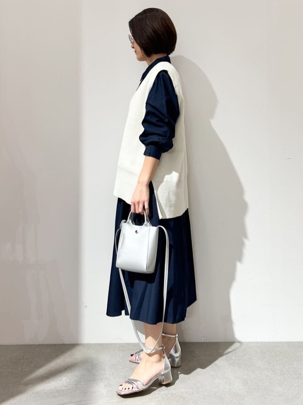 ホワイト系のベスト、ブルー系のワンピース、シルバー系のサンダルを着用したレディースの春コーディネートの2枚目の写真