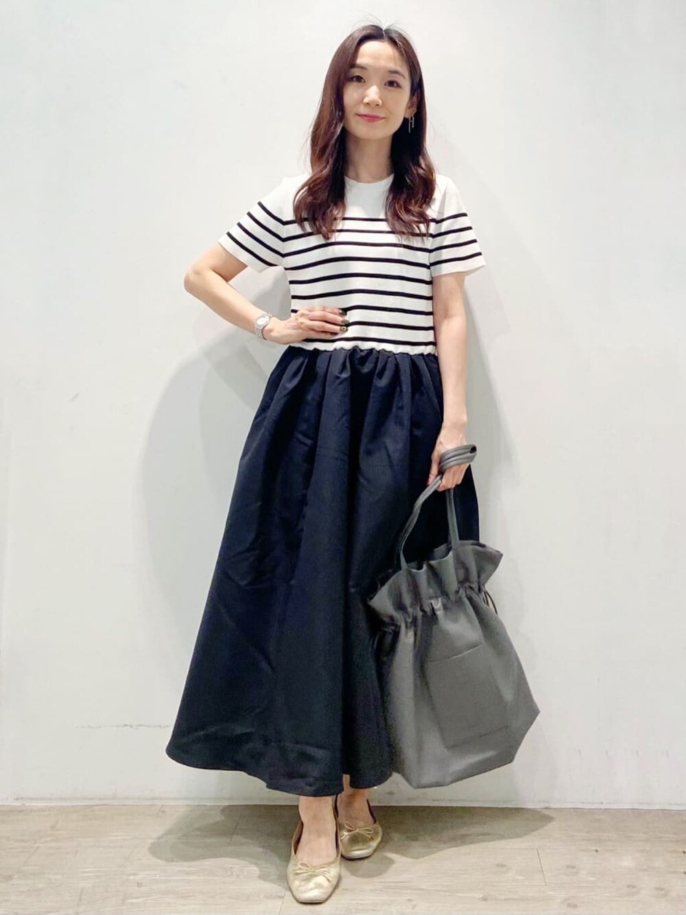 グレー系のトートバッグ、ブラック系のワンピース、ゴールド系のその他シューズを着用したレディースの夏コーディネートの2枚目の写真