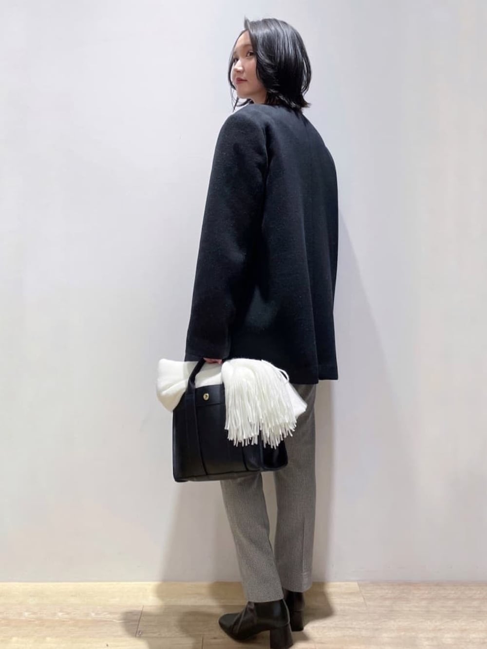 ブラック系のノーカラーコート、イエロー系のニット/セーター、ブラック系のトートバッグを着用したレディースの秋コーディネートの3枚目の写真