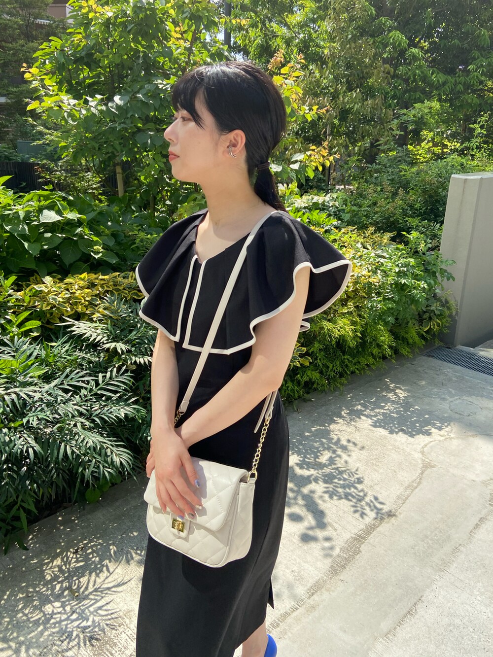 ブラック系のワンピース、ブルー系のパンプス、ホワイト系のショルダーバッグを着用したレディースの春コーディネートの2枚目の写真