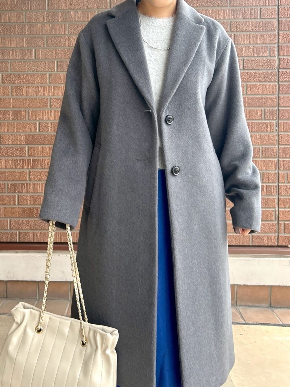 ブルー系のスカート、グレー系のニット/セーター、グレー系のチェスターコートを着用したレディースの秋コーディネートの5枚目の写真