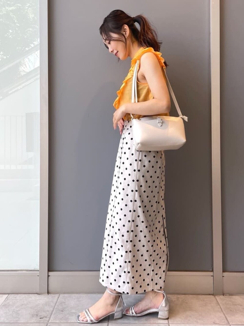 ホワイト系のショルダーバッグ、ベージュ系のスカート、シルバー系のサンダルを着用したレディースの夏コーディネートの2枚目の写真