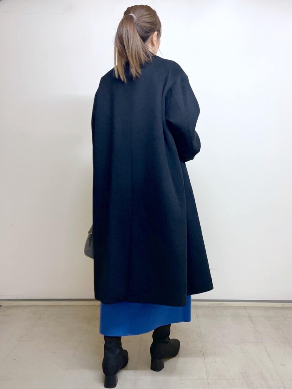 ブラック系のチェスターコート、ブルー系のスカート、ブラック系のブーツを着用したレディースの冬コーディネートの3枚目の写真