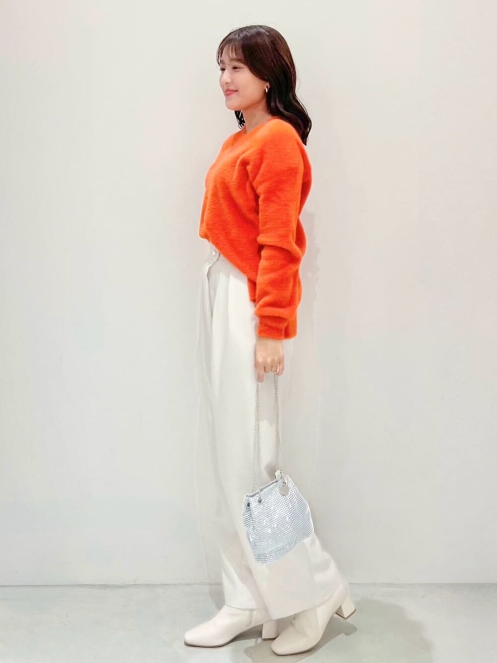 オレンジ系のニット/セーター、ホワイト系のその他パンツ、ホワイト系のショルダーバッグを着用したレディースの秋コーディネートの2枚目の写真