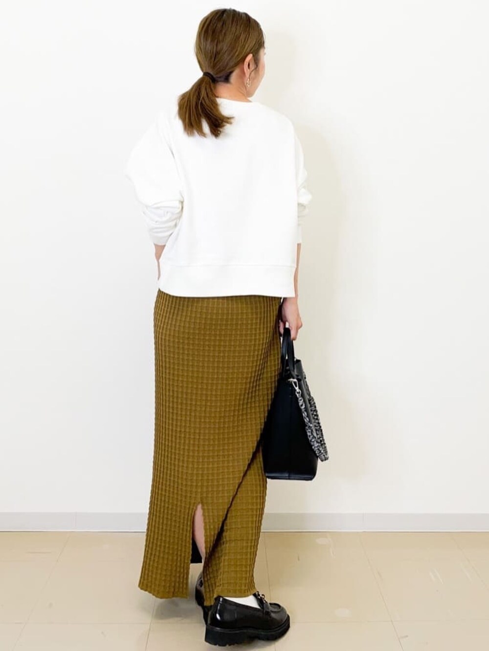 イエロー系のスカート、ブラック系のショルダーバッグ、ブラック系のパンプスを着用したレディースの秋コーディネートの4枚目の写真