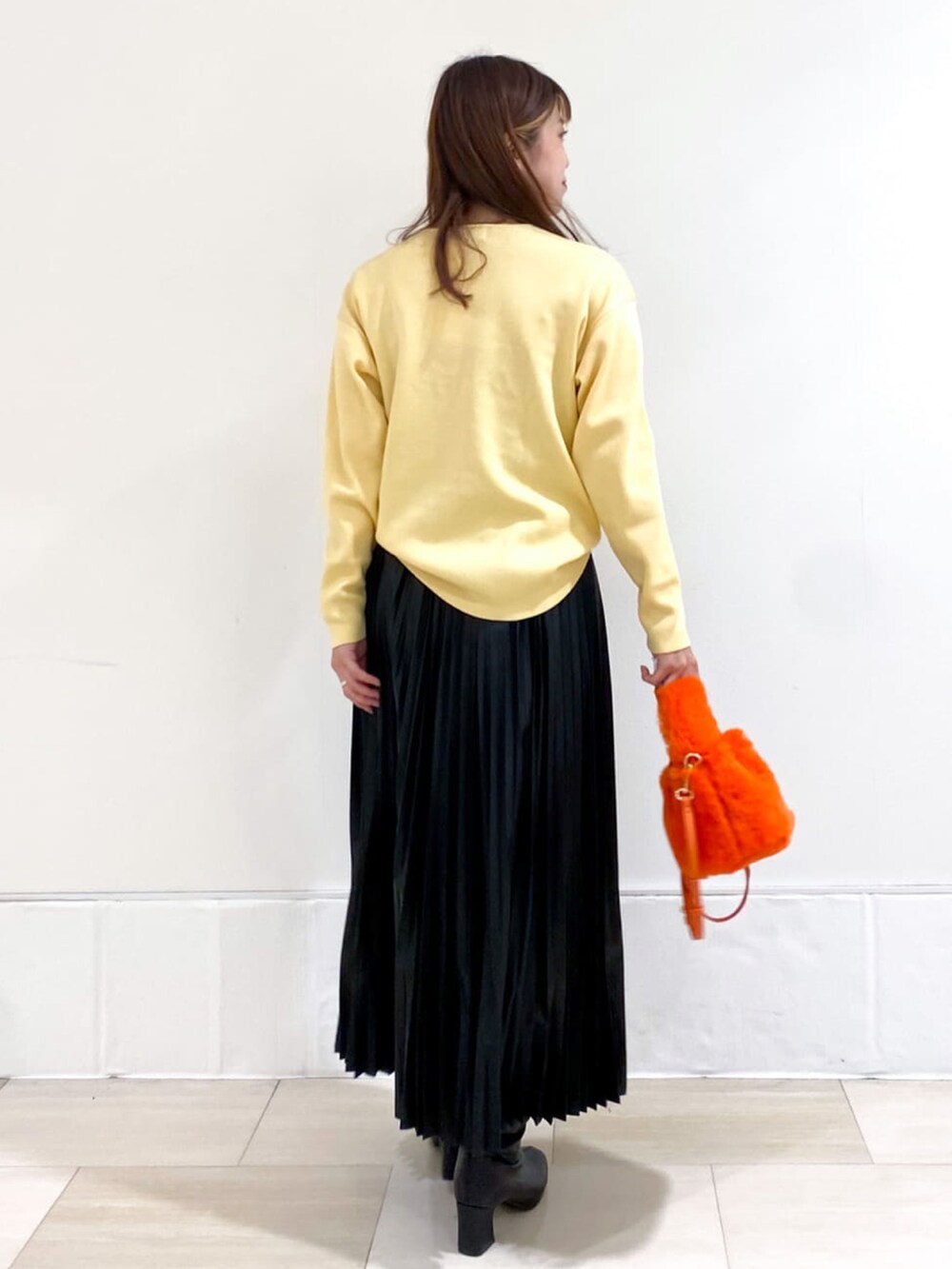 イエロー系のニット/セーター、ブラック系のスカート、オレンジ系のショルダーバッグを着用したレディースの秋コーディネートの3枚目の写真
