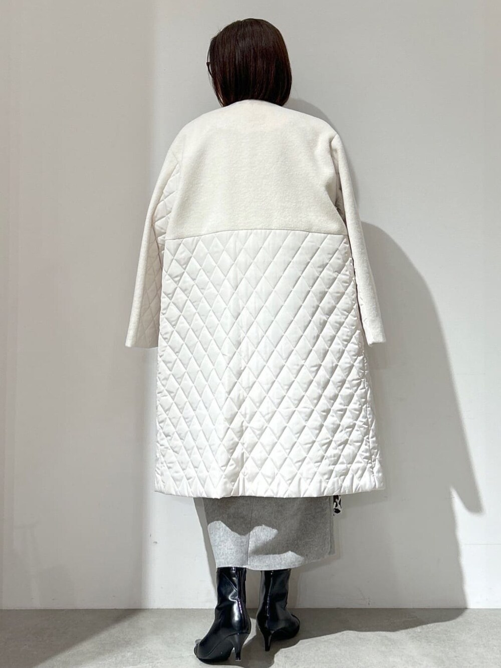 ホワイト系のノーカラーコート、グレー系のスカート、ブラック系のショルダーバッグを着用したレディースの秋コーディネートの4枚目の写真