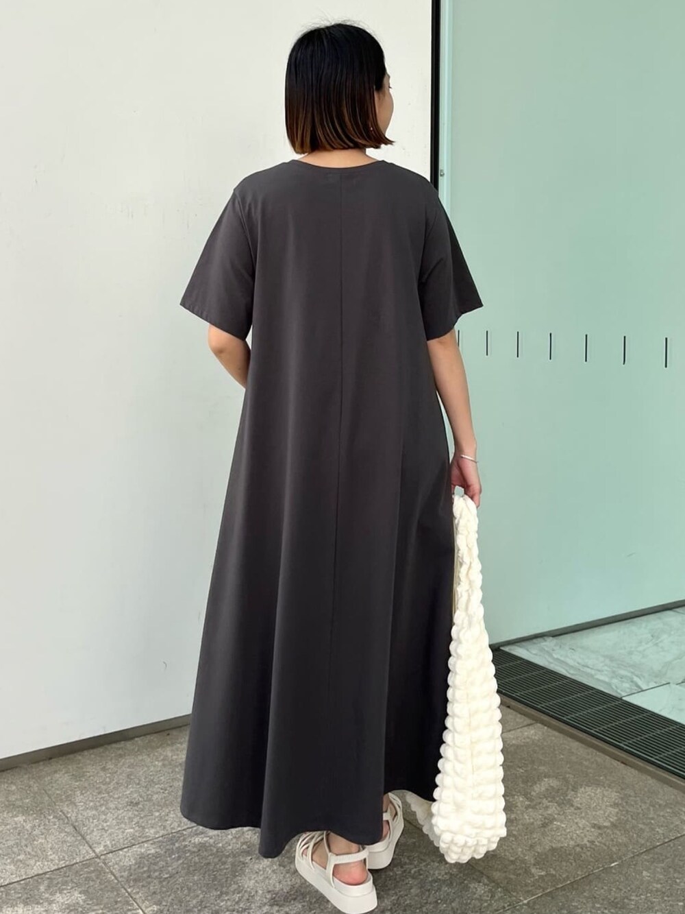 グレー系のワンピース、ホワイト系のサンダル、ホワイト系のショルダーバッグを着用したレディースの春コーディネートの2枚目の写真