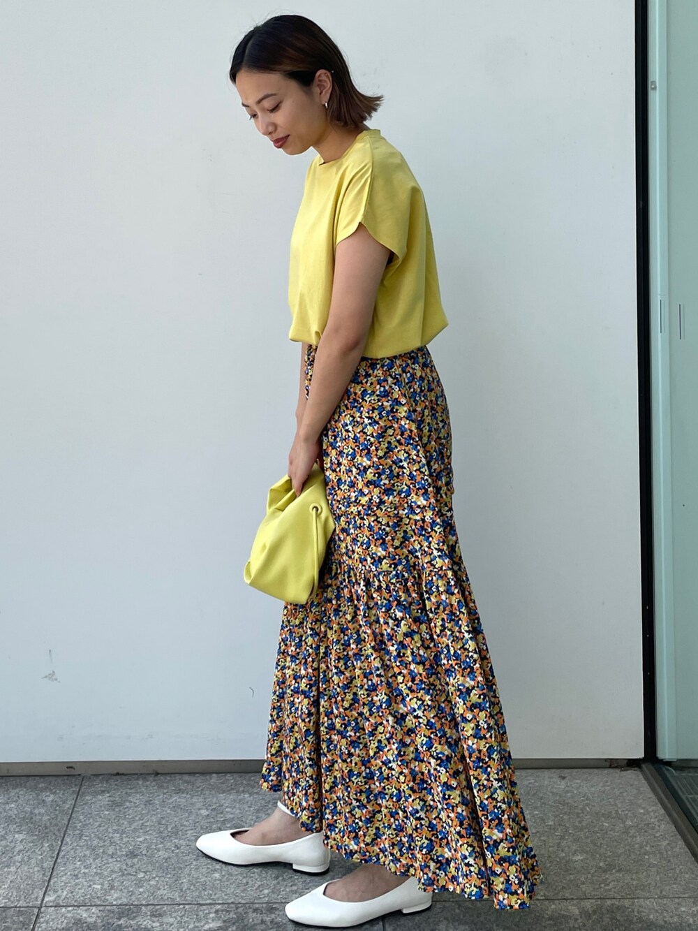 イエロー系のTシャツ/カットソー、オレンジ系のスカート、ホワイト系のパンプスを着用したレディースの夏コーディネートの2枚目の写真