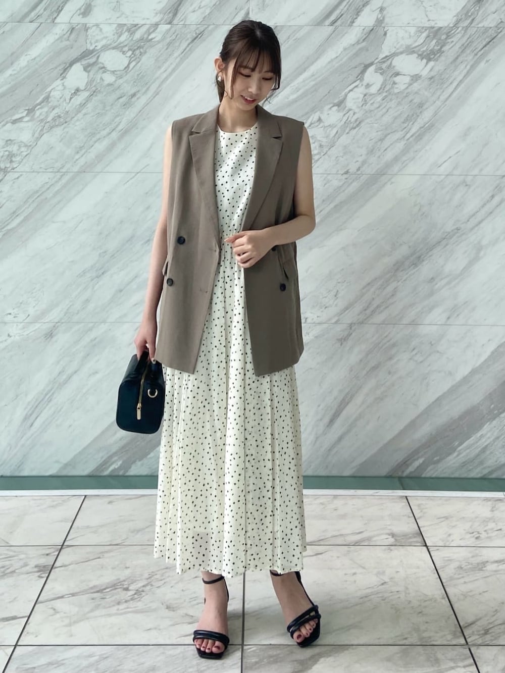 ブラウン系のベスト、ホワイト系のワンピース、ブラック系のサンダルを着用したレディースの春コーディネートの3枚目の写真